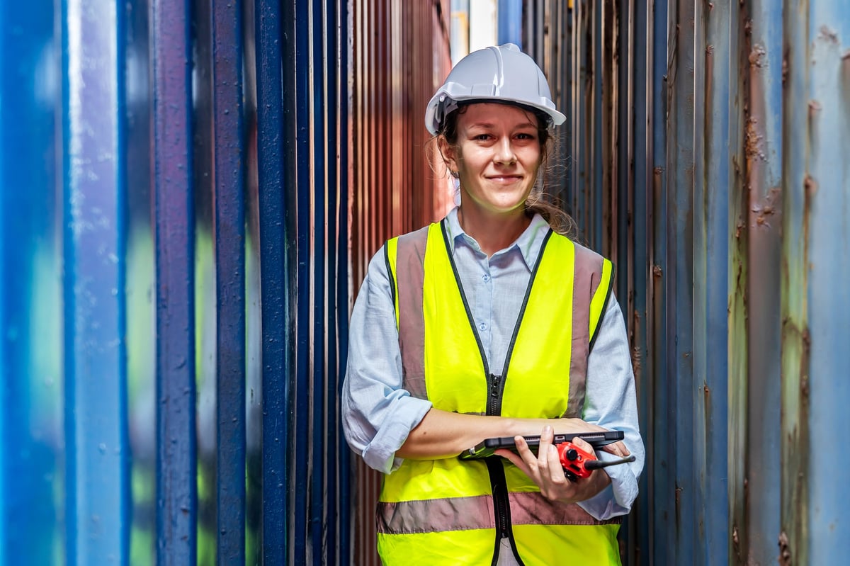 A female construction worker in a yellow vest using a walkie-talkie