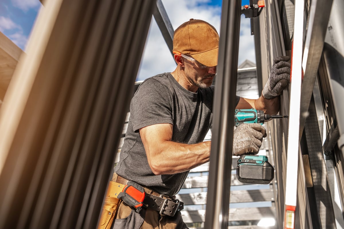 A construction worker installing wall panels with a power tool while wearing protective gear