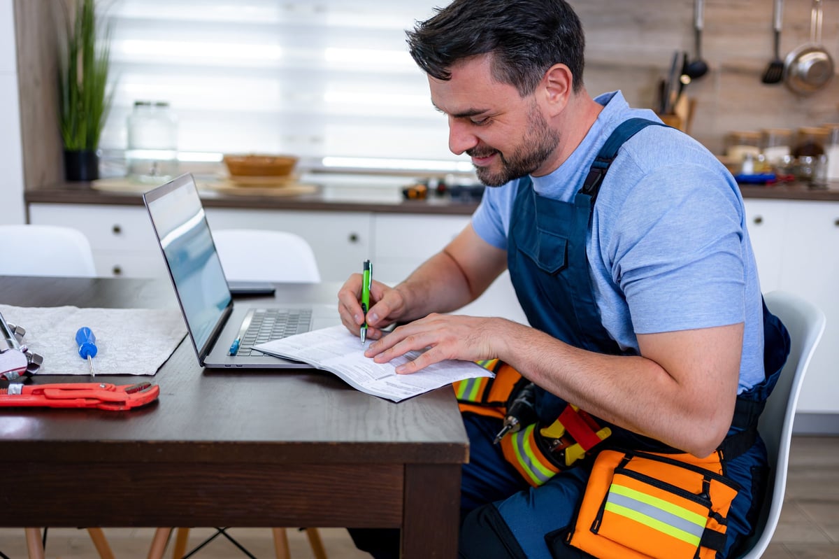 A handyman documenting a household repair at a kitchen table with a laptop and tools