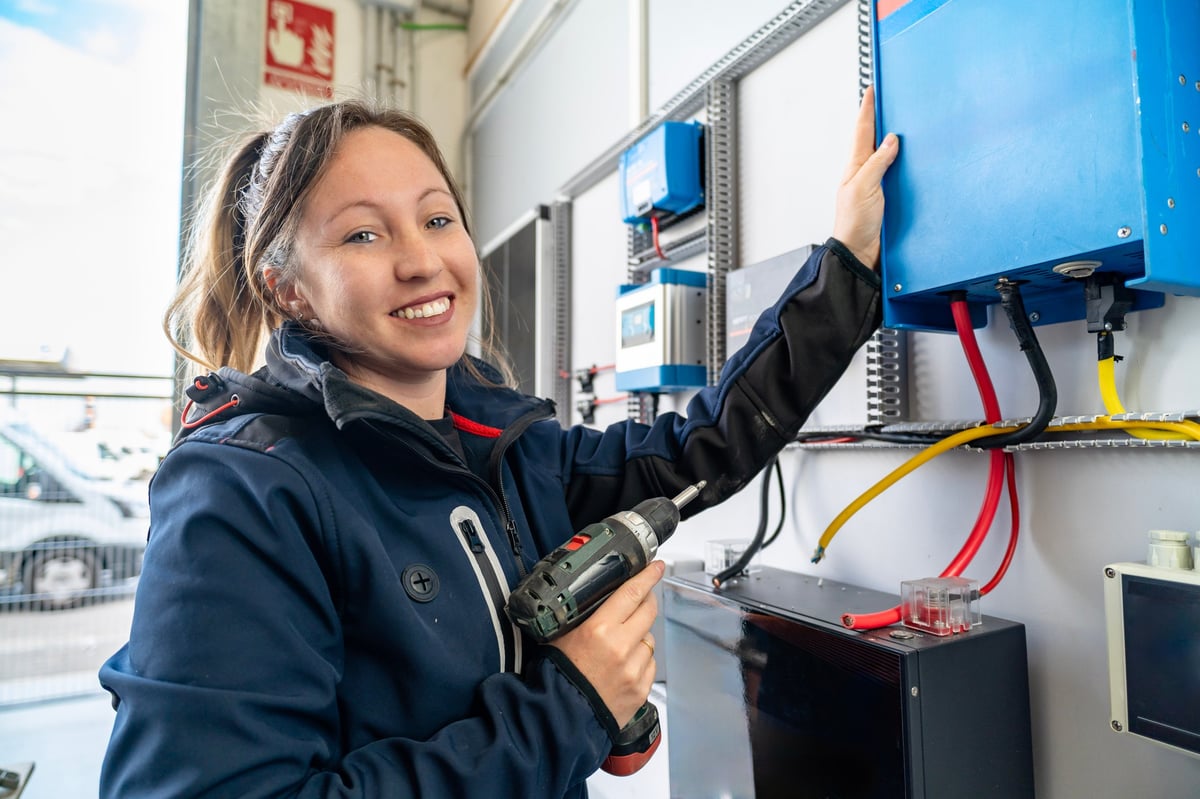 A smiling tradesperson checking a power inverter for a renewable energy installation