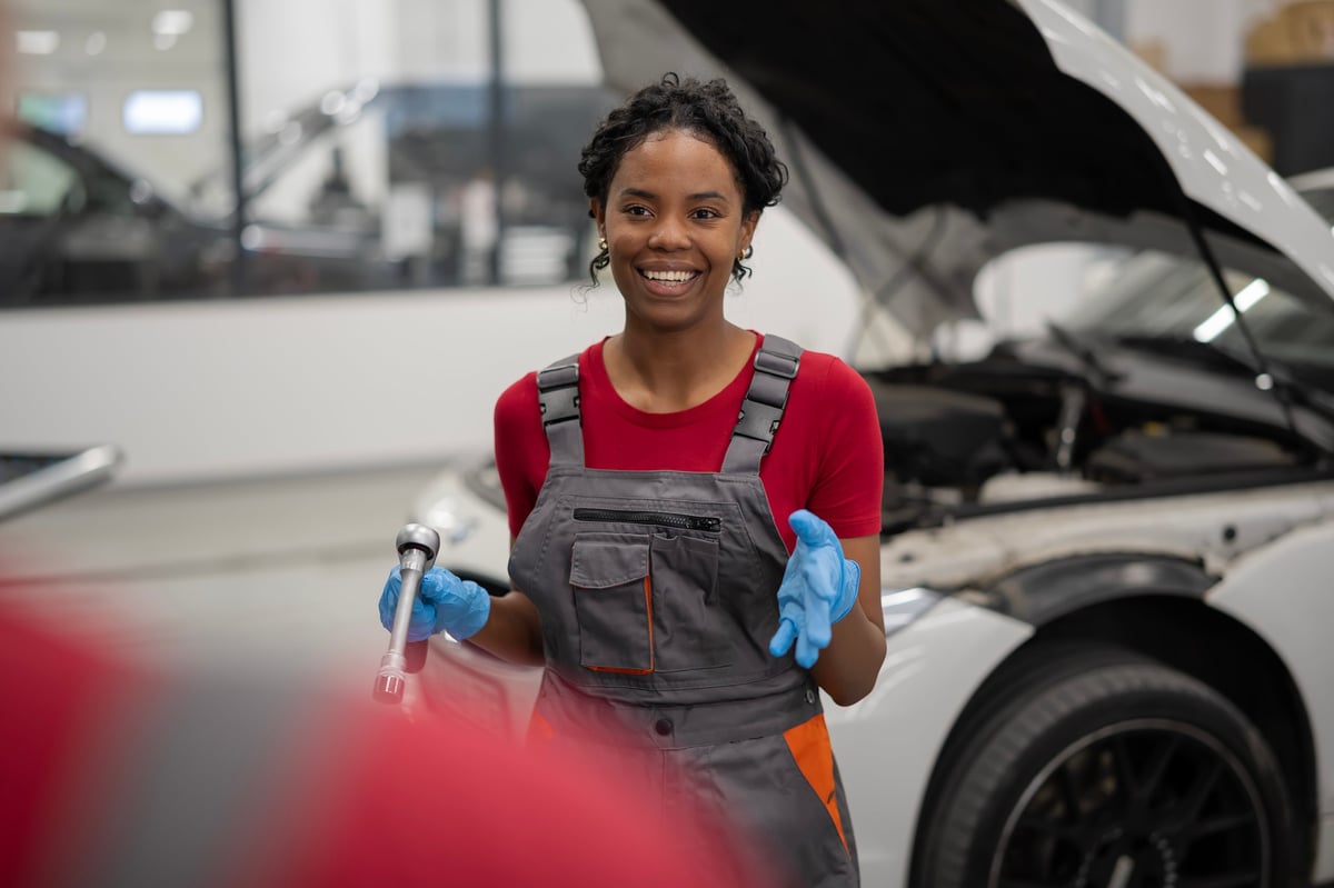 A smiling tradesperson apprentice holding a wrench in a garage